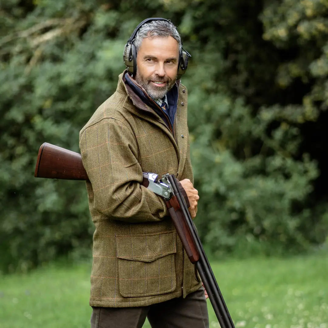 Man in a brown Maverick Waterproof Tweed Jacket holding a shotgun outdoors