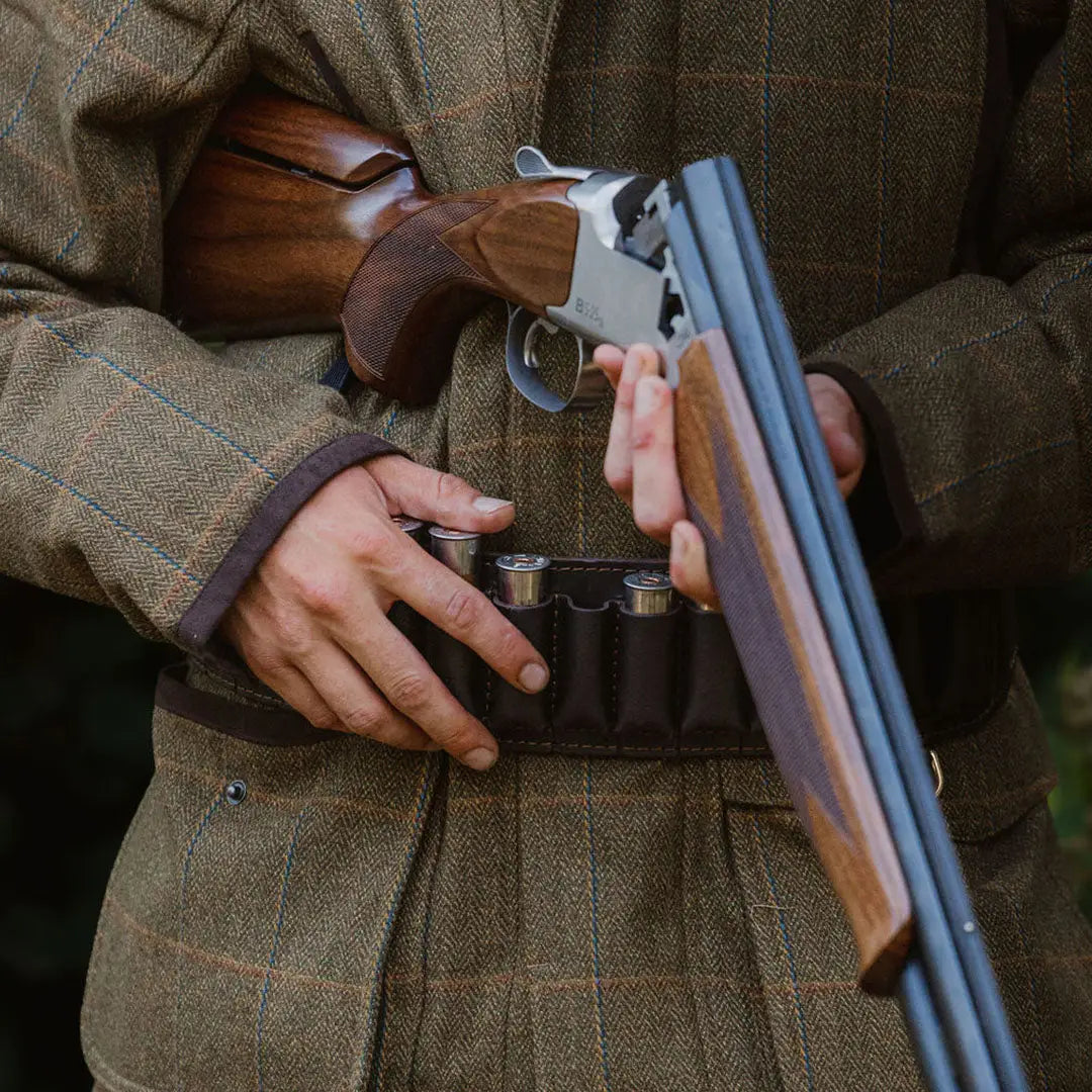 Double-barreled shotgun with a wooden stock and metal barrels beside a Forest Maverick Waterproof Tweed Jacket