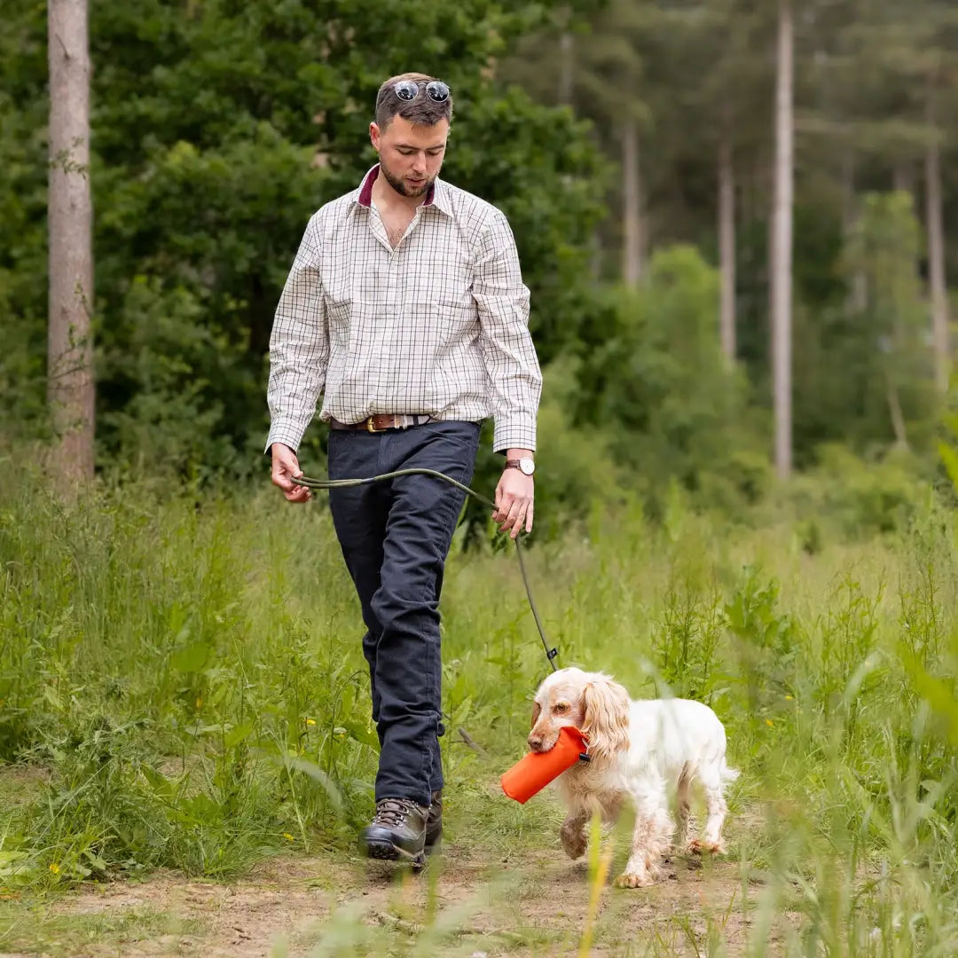 Man in Forest Moleskin Jeans walking a small white dog in a grassy area