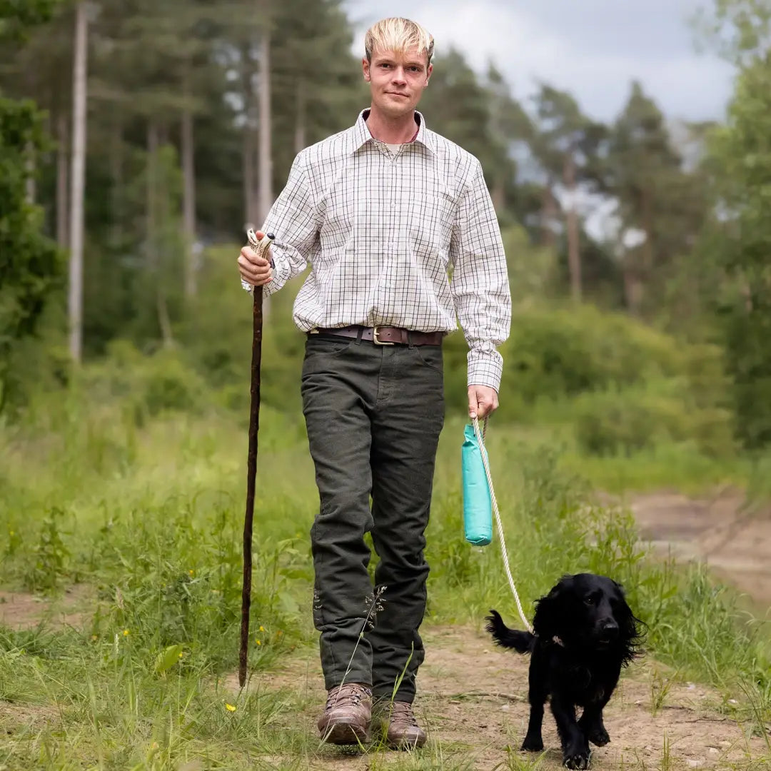 Man in Forest Moleskin Jeans walks black dog down dirt path with a walking stick