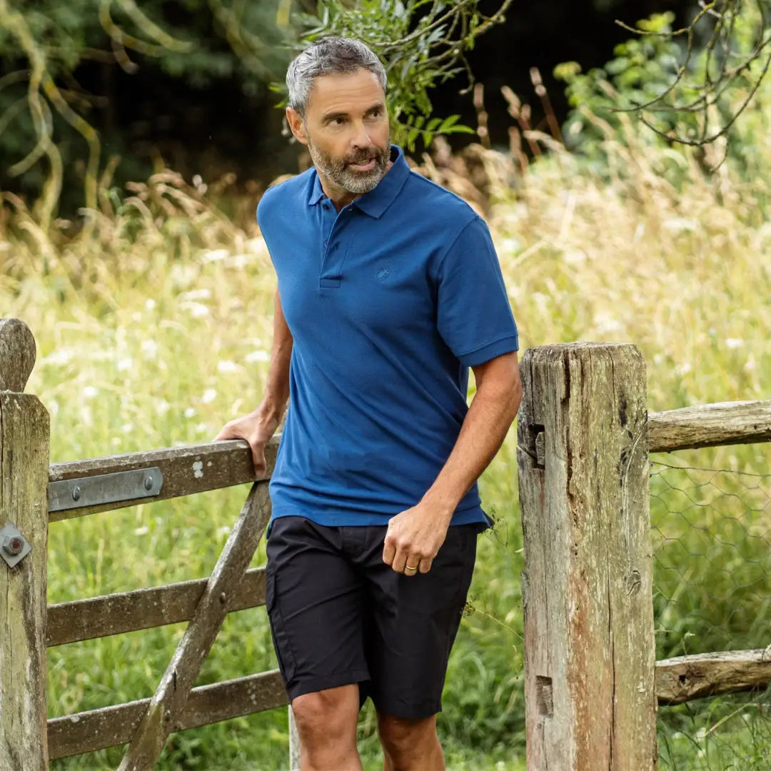 Middle-aged man in blue forest pique polo shirt and black shorts, stylish look