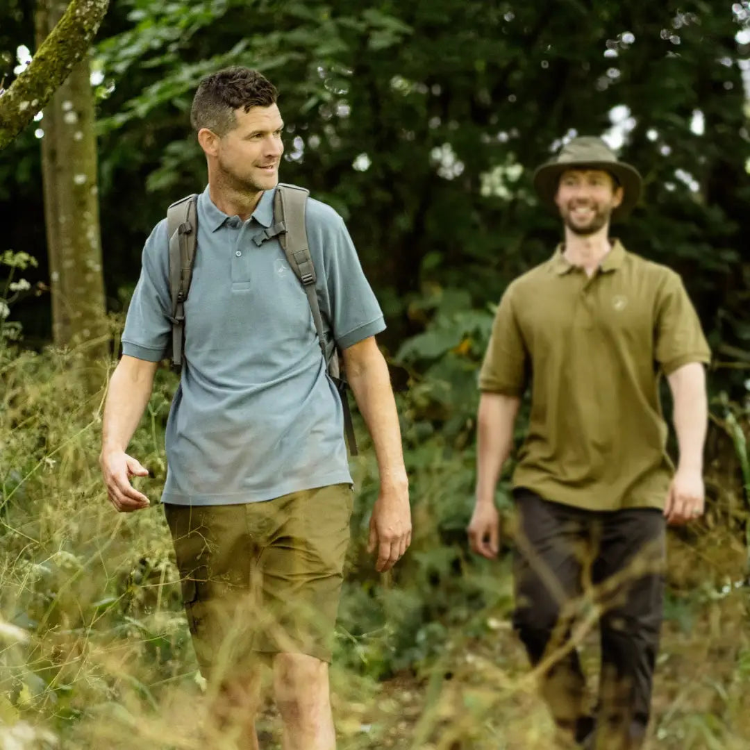 Two men wearing a Forest Pique Polo Shirt hike through a lush, green forest