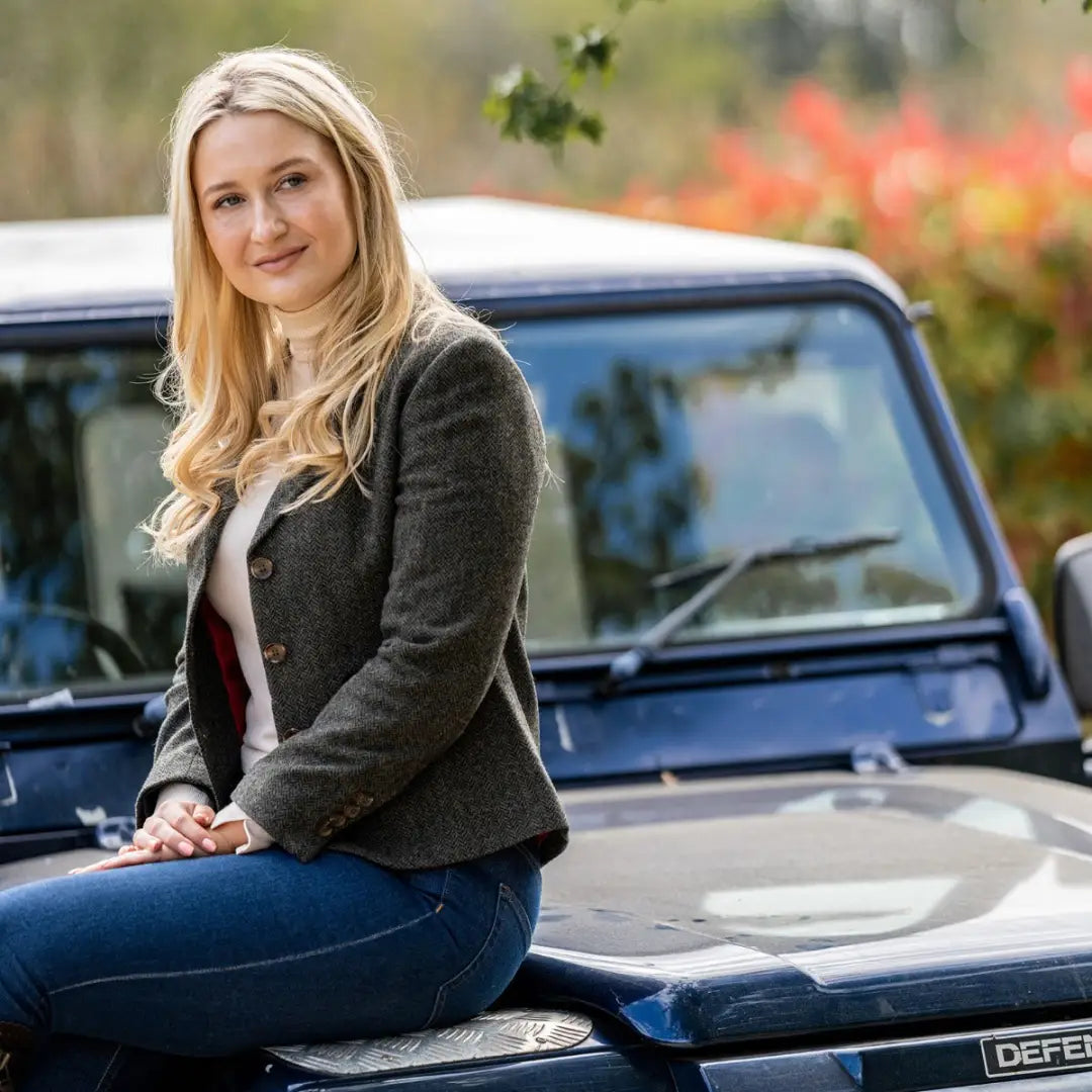 Woman with long blonde hair in a Polly Tweed Blazer sitting on a blue car hood