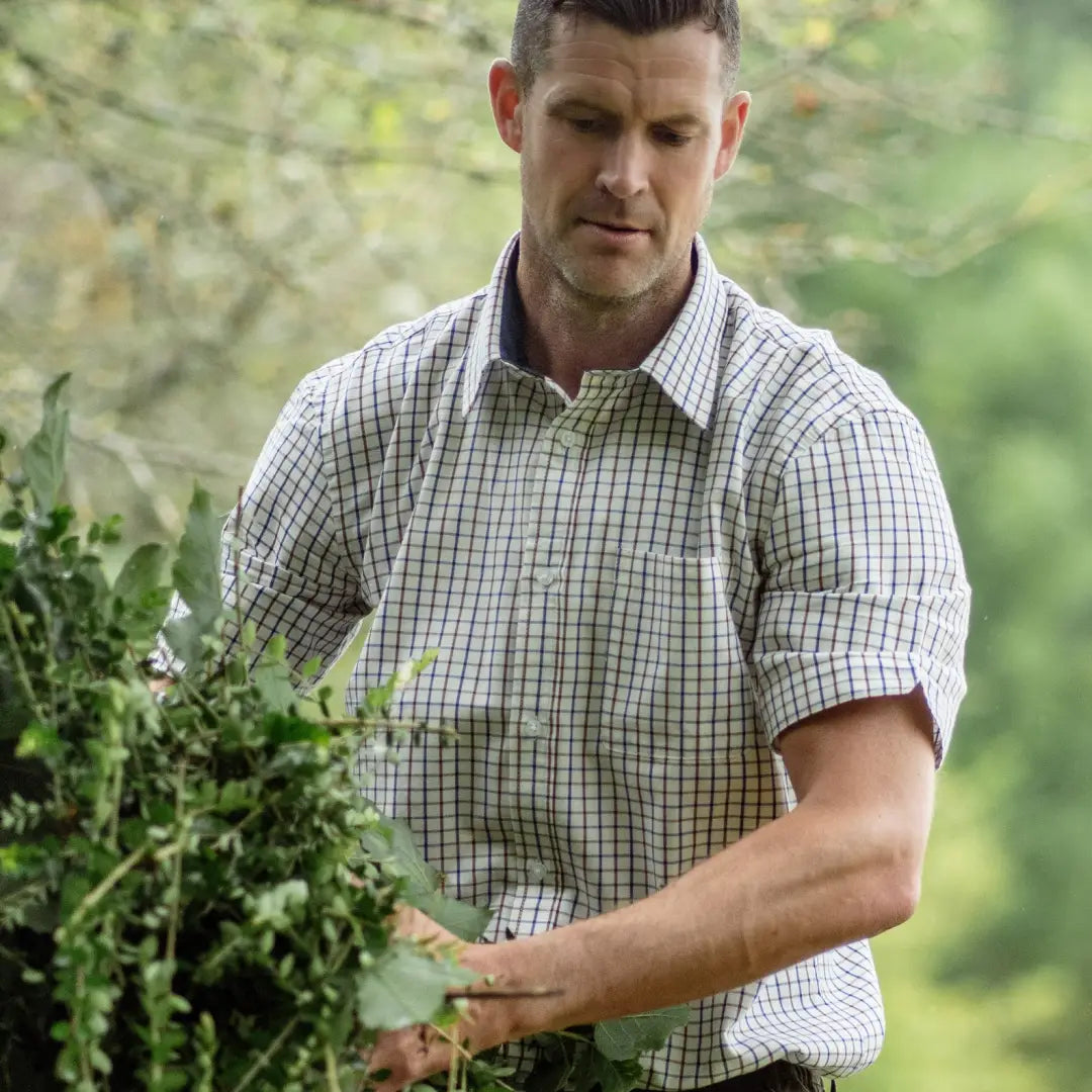 Man in a checkered shirt examining plants outdoors, showcasing a forest short sleeved style