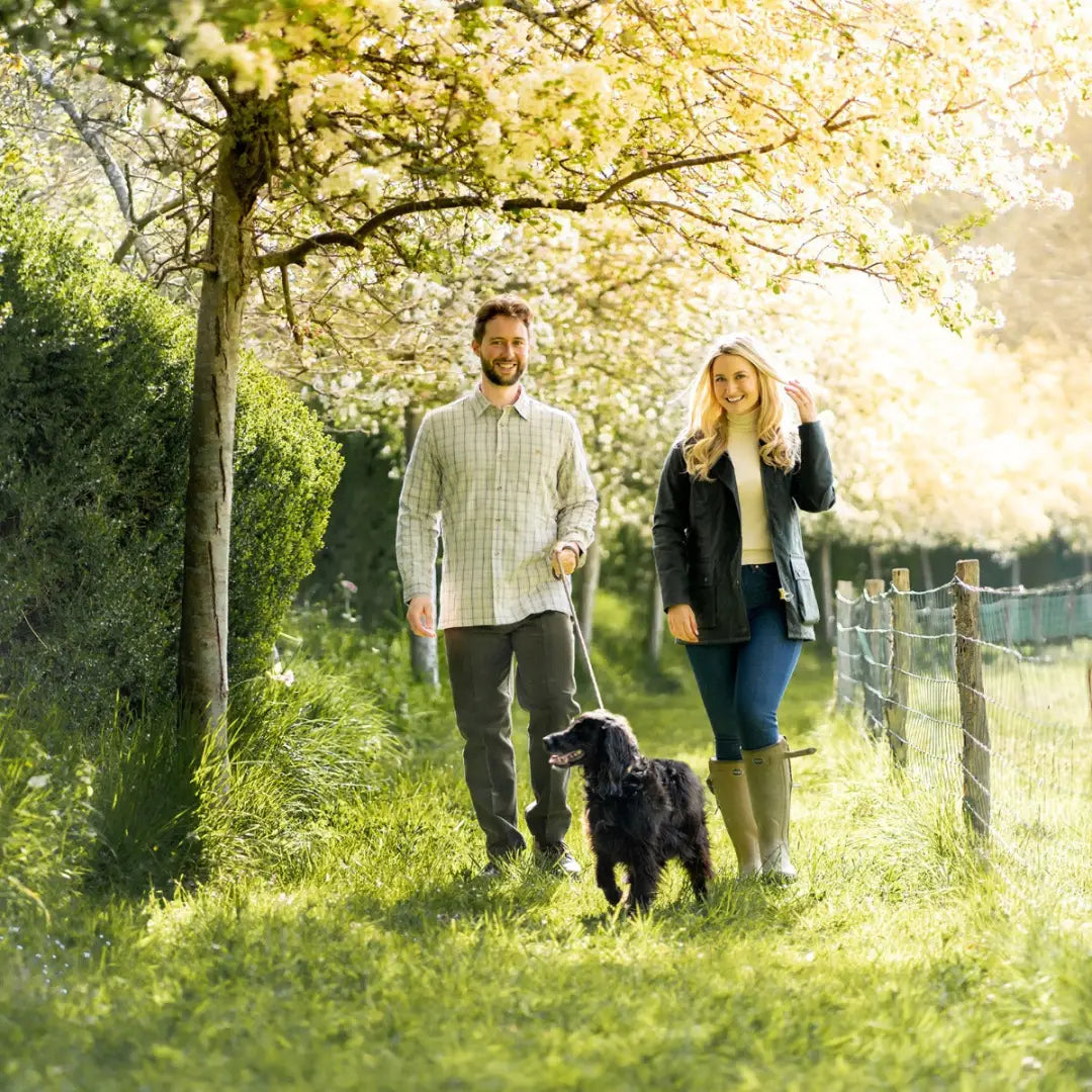 Couple in New Forest fleece lined shirt walking black dog under blossoming trees