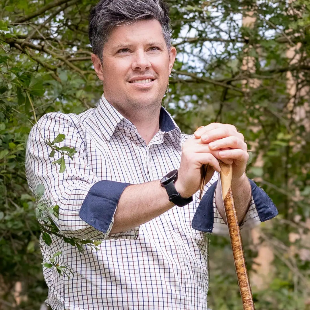 Man in a checkered tattersall shirt holds a wooden walking stick outdoors, New Forest Premium