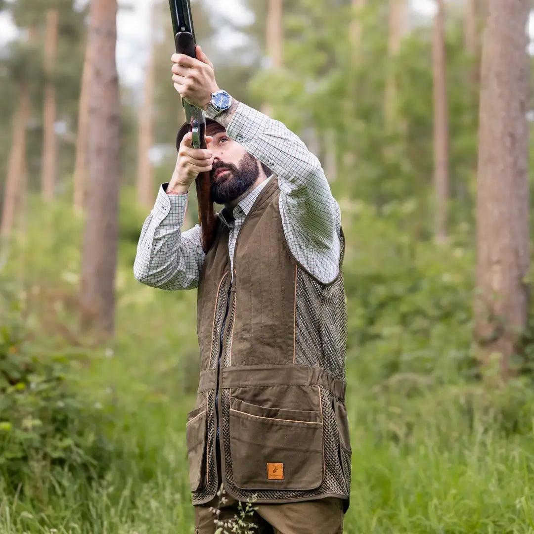 Man in forest aiming shotgun, showcasing a New Forest Premium Tattersall Shirt