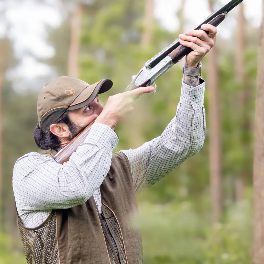 Person in a checkered Premium Tattersall Shirt aiming a shotgun skyward