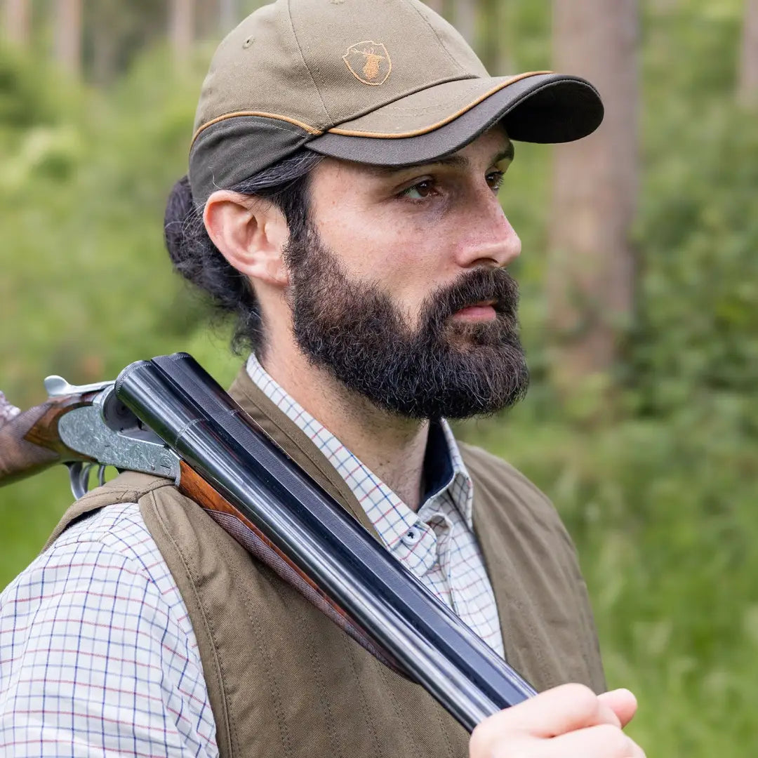 Bearded guy in a cap and vest with a shotgun, rocking a Premium Tattersall Shirt