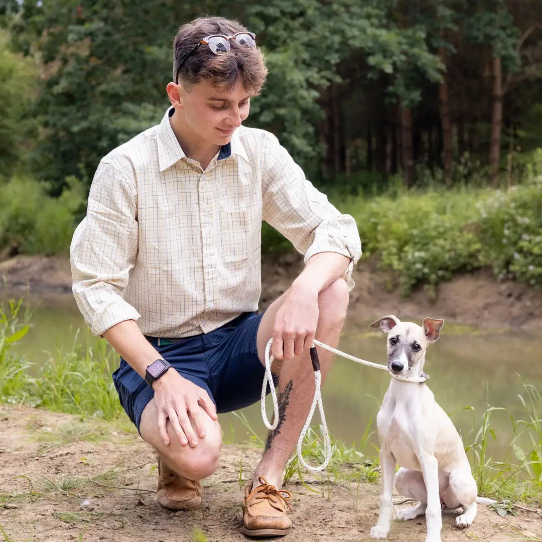 Man kneeling by water with small white dog wearing New Forest Premium Tattersall Shirt