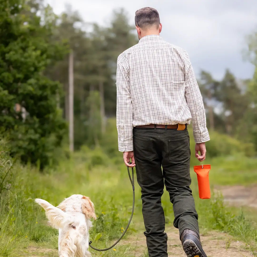 Man in a New Forest Tattersall Shirt walking a small white dog with an orange container