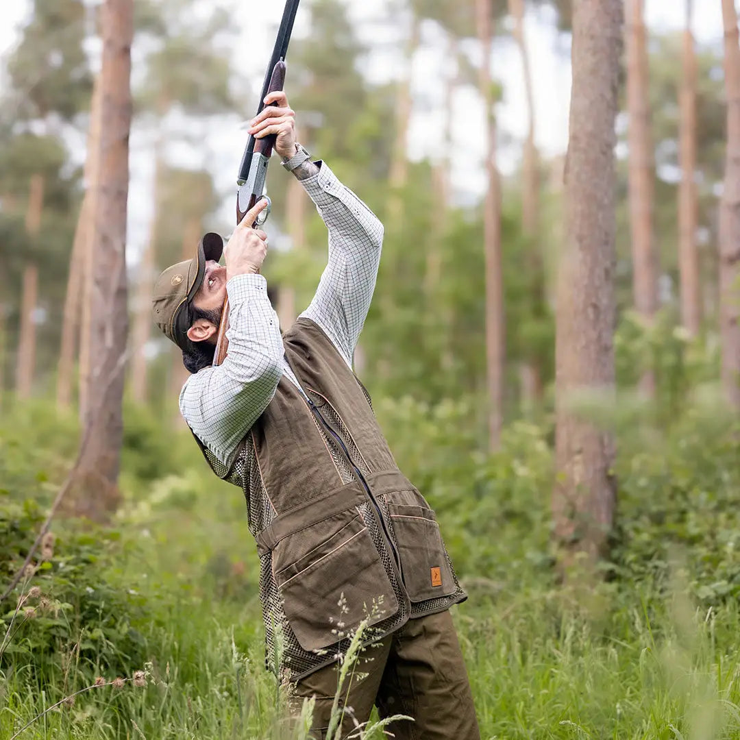 Man aiming a shotgun in the forest wearing a stylish Forest Skeet Vest