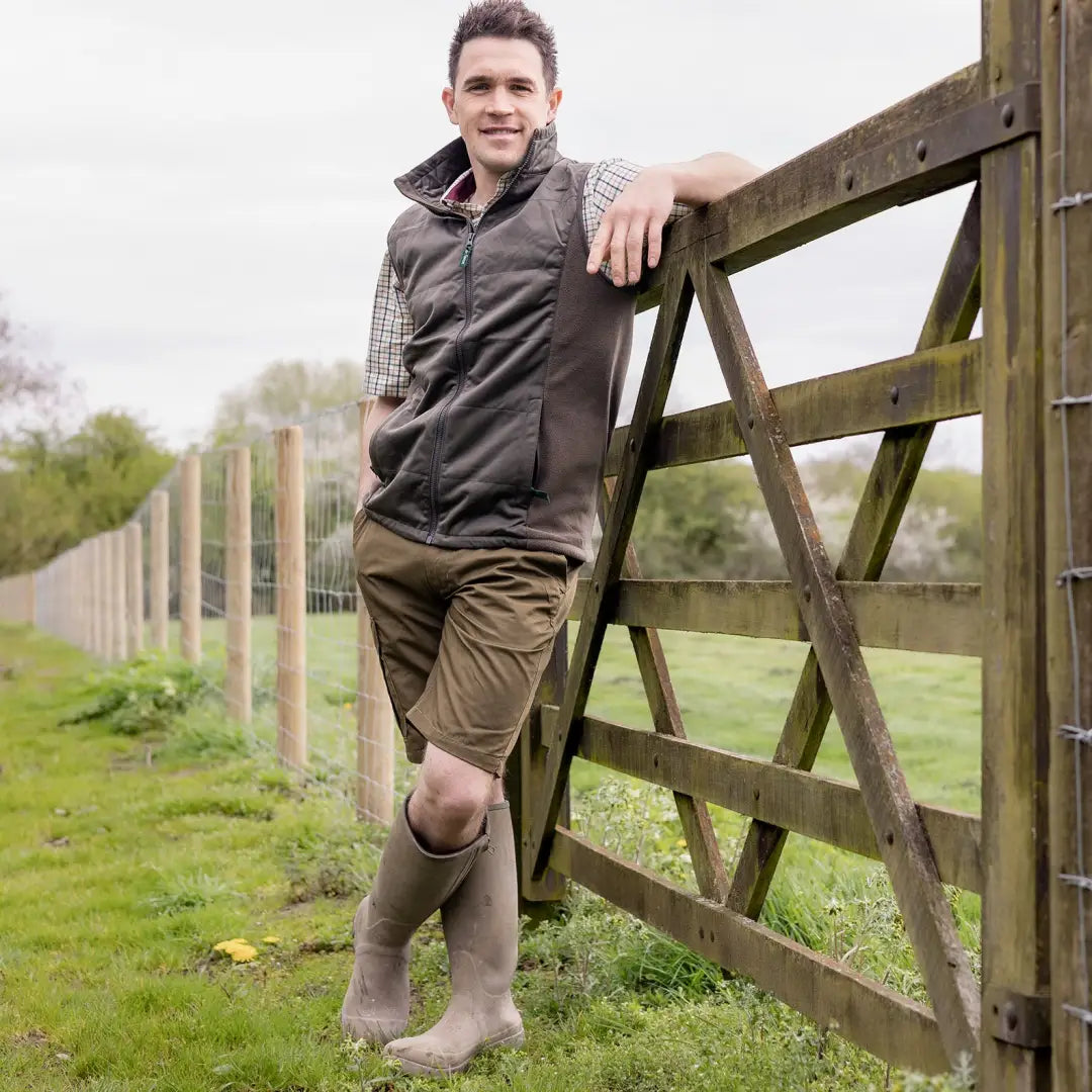 Man in New Forest Trail Shorts leaning against a wooden gate in a rural setting