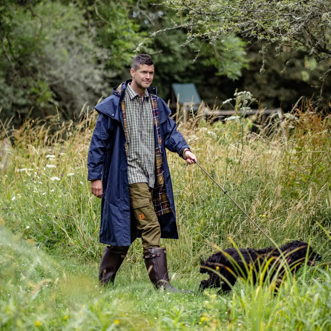 Man in a blue coat walking his dog in tall grass wearing New Forest Trail Trousers