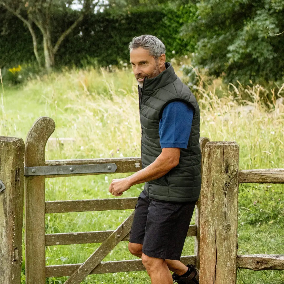 Middle-aged man in a dark vest and shorts by a gate showcasing the Forest Trek Gilet