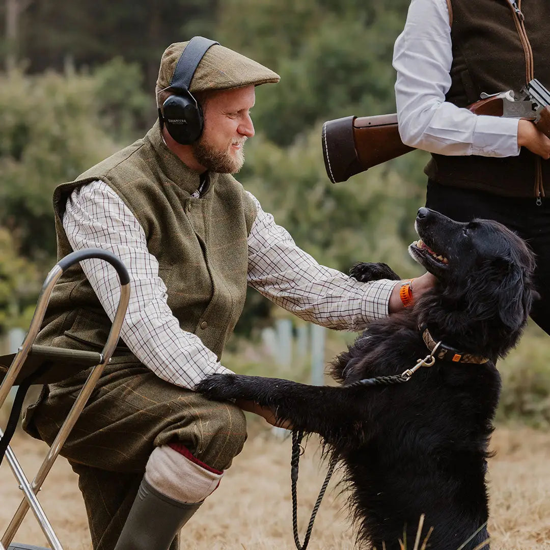 Man in traditional hunting attire with a black dog wearing stylish Tweed Breeks