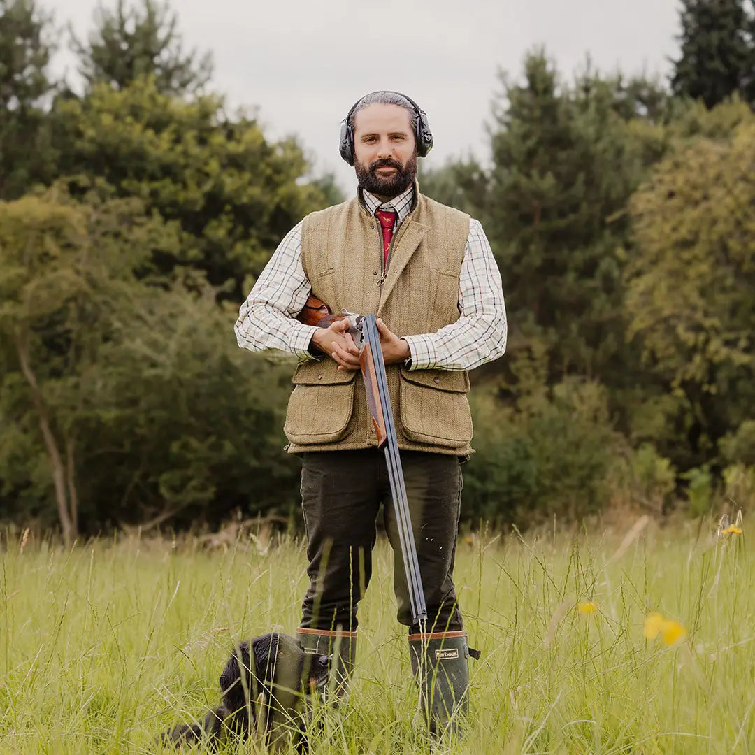 Man in hunting attire with shotgun showcasing a stylish Tweed Gilet for country clothing