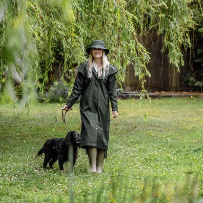 Woman in New Forest Victoria Cape walking black dog under willow tree in wet weather