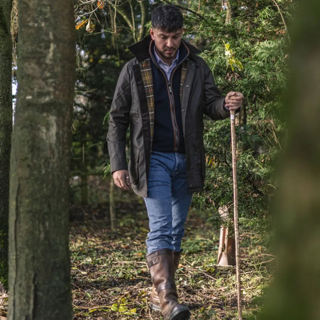 Man in a New Forest Woodsman Wax Jacket walking through the woods with a stick