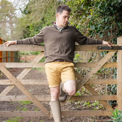 Man in casual outfit leaning on wooden gate wearing New Forest zip neck jumper