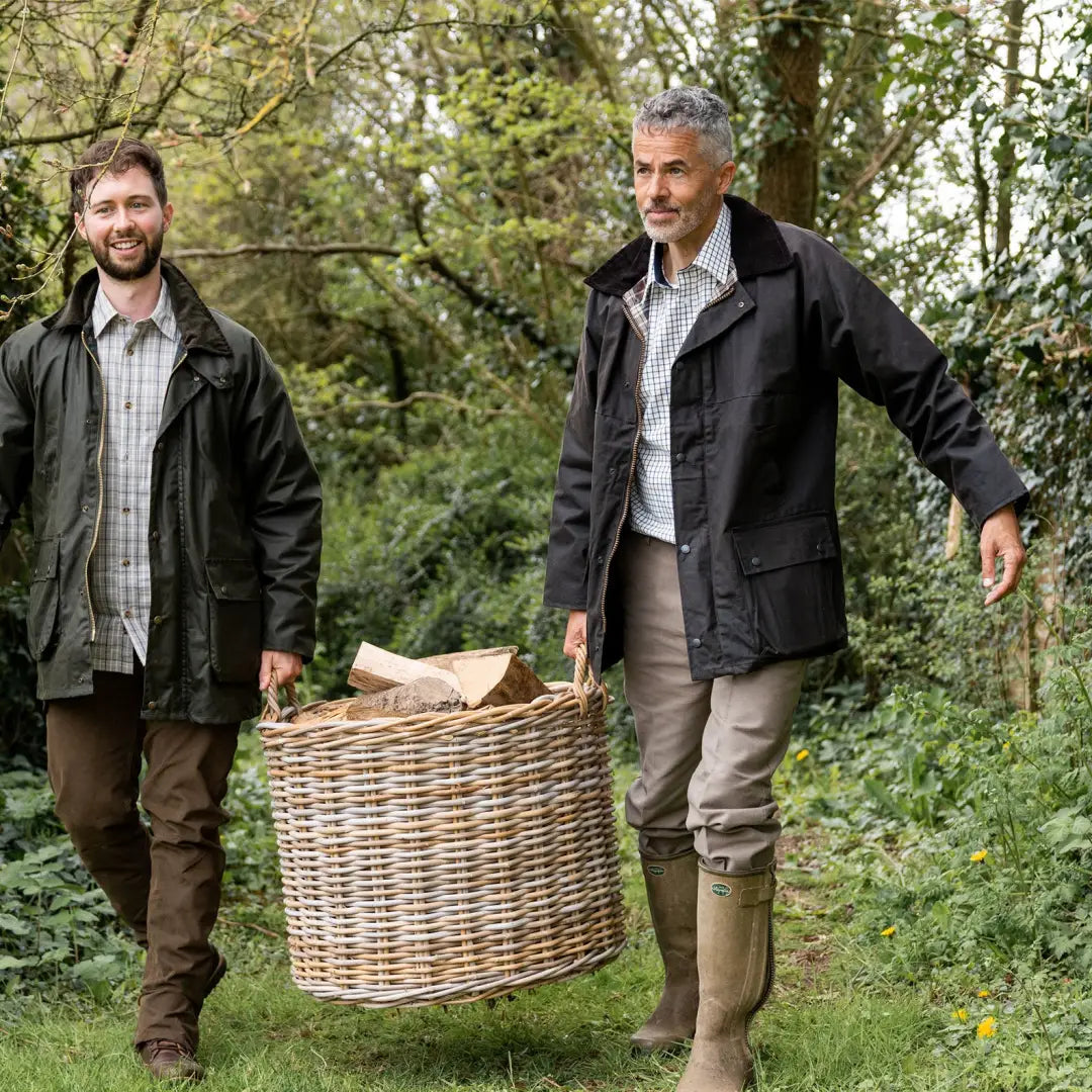 Two men in a Padded Wax Jacket carry a wicker basket through the woods