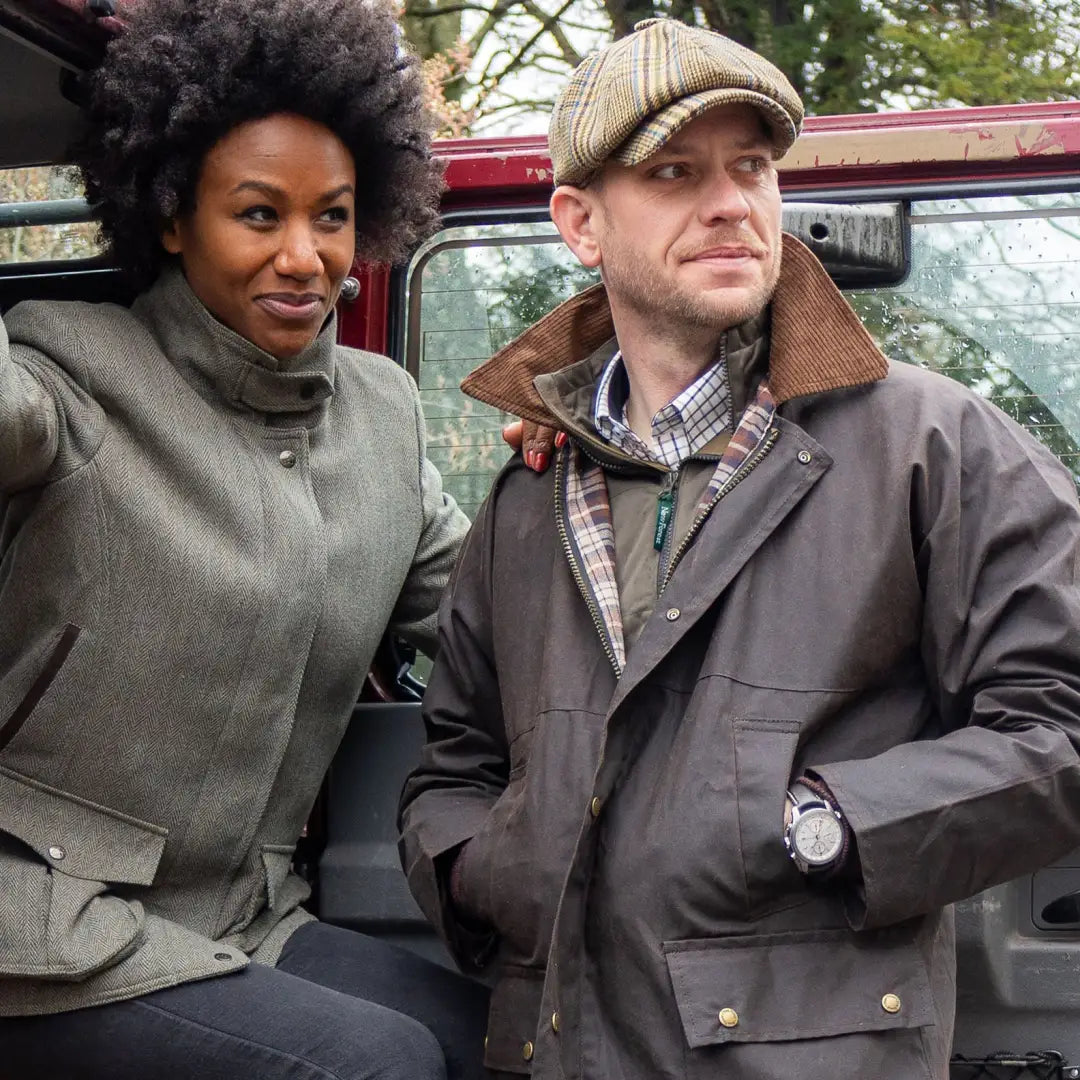 Two people in winter coats showcase a stylish padded wax jacket by a vehicle