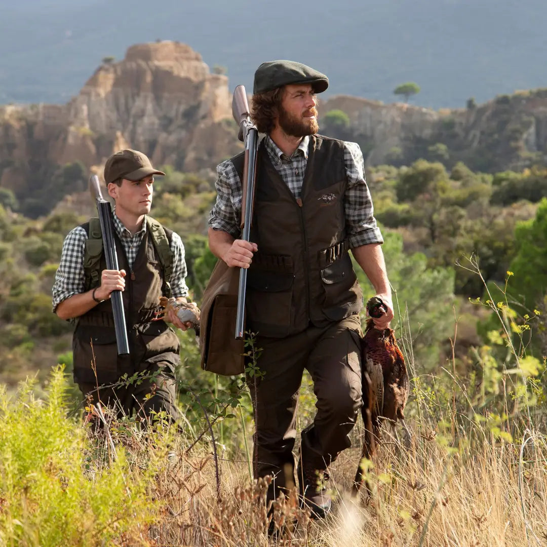 Two hunters in Percussion Tradition Trousers with rifles and a hunting dog in tall grass