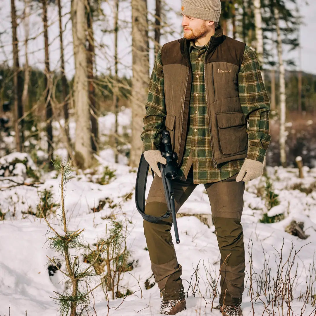 Man in winter country clothing with rifle in snowy forest, showcasing Pinewood Caribou Hunt Trousers