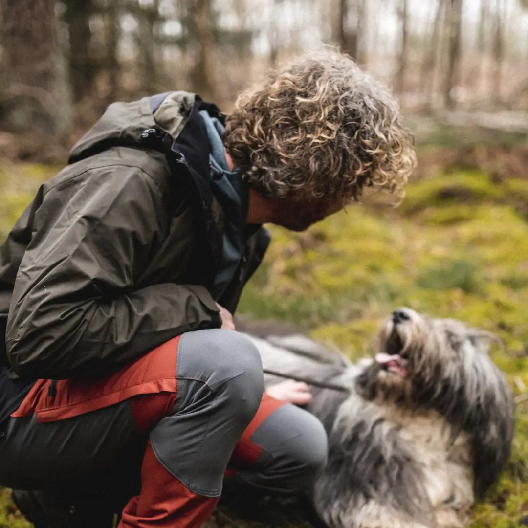 Person with curly hair playing with shaggy dog in forest wearing Pinewood Dog Sports Jacket