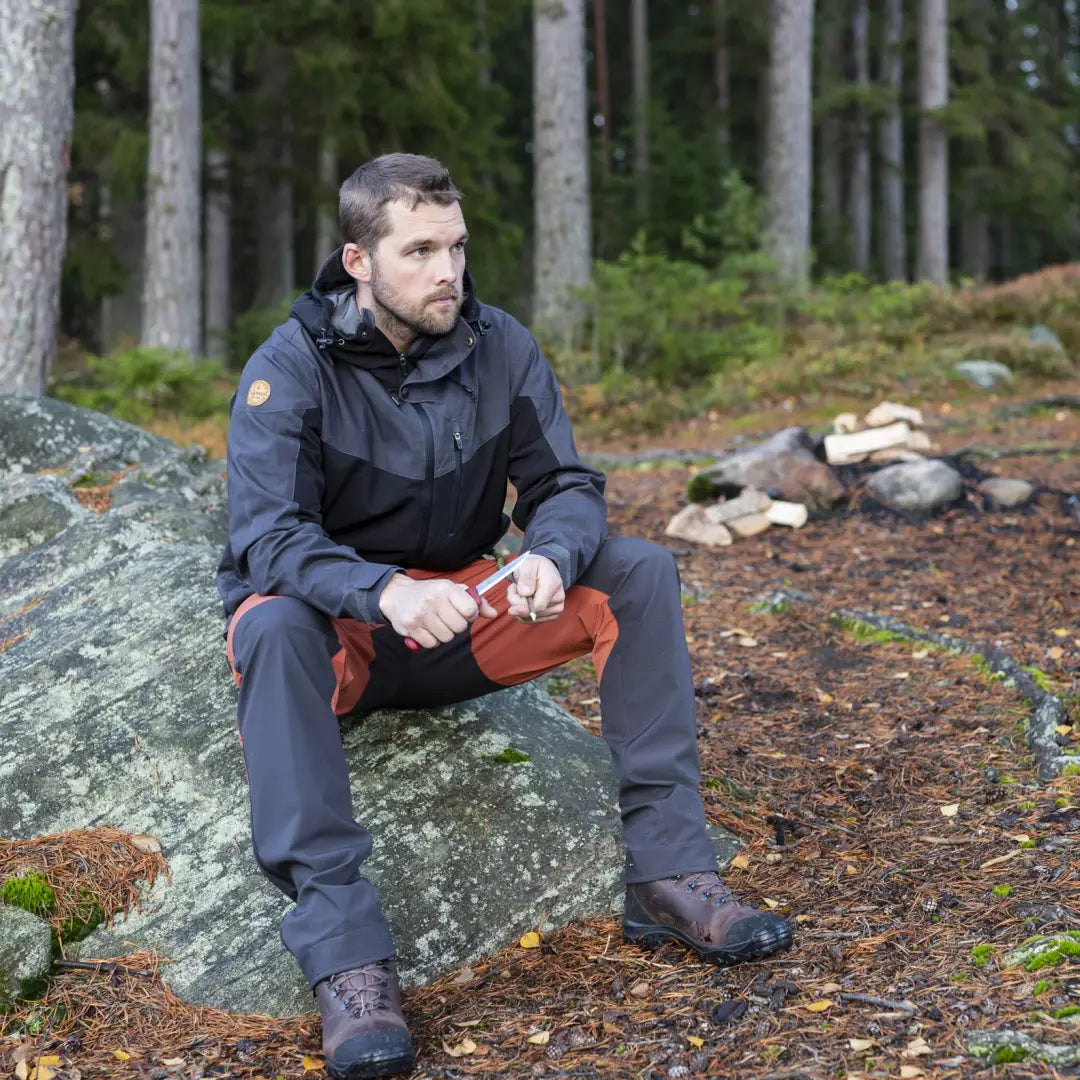 Man in outdoor gear wearing Pinewood Finnveden Hybrid Extreme Jacket on a rock