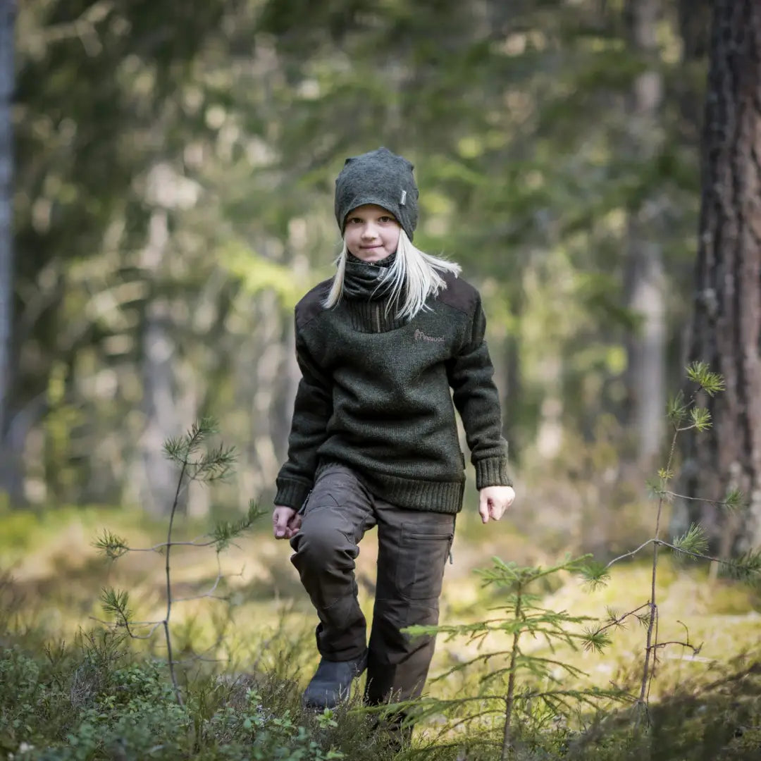 Person in a Pinewood Kids Hurricane Sweater strolling through a snowy forest