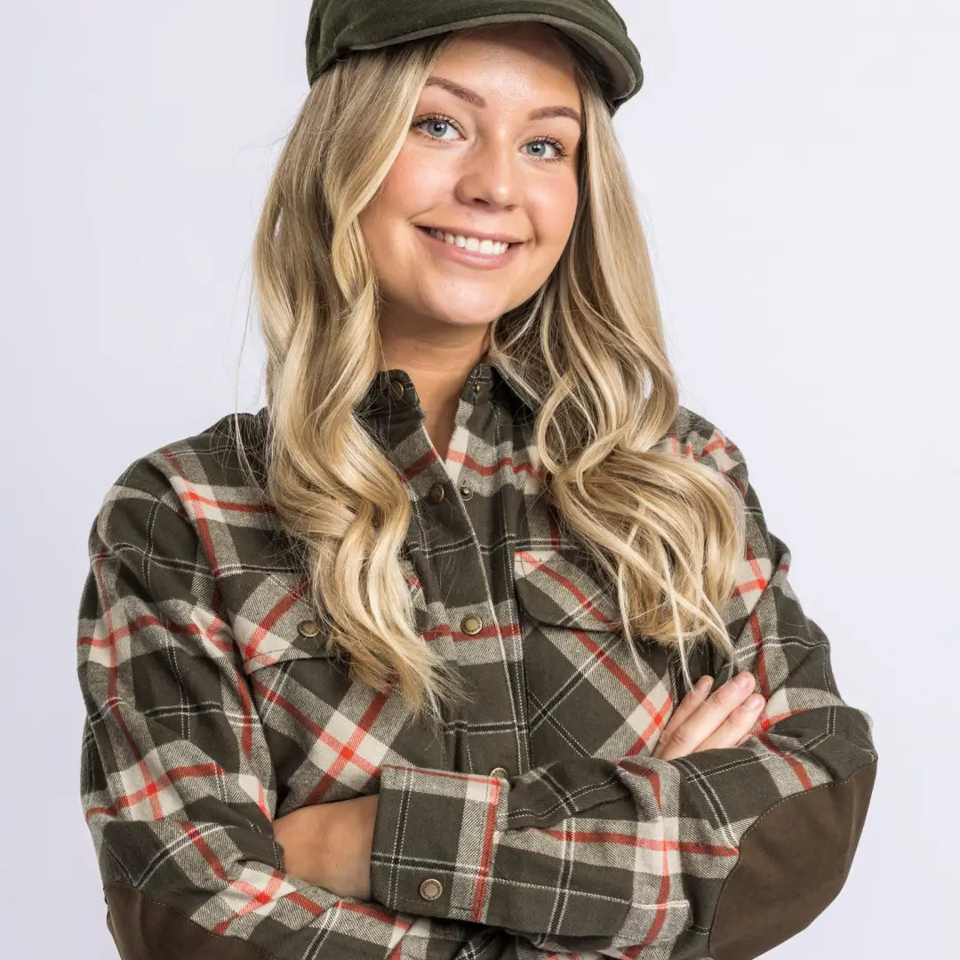 Smiling woman in a plaid flannel shirt and newsboy cap rocking country clothing outdoors