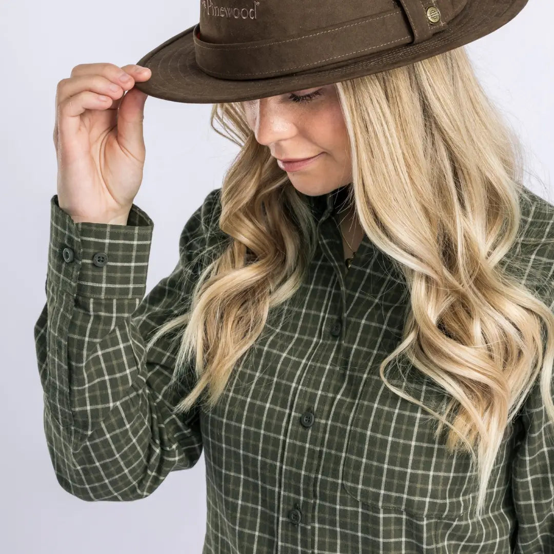 Brown wide-brimmed hat touched by a person in a green plaid Pinewood Ladies Nydala shirt outdoors