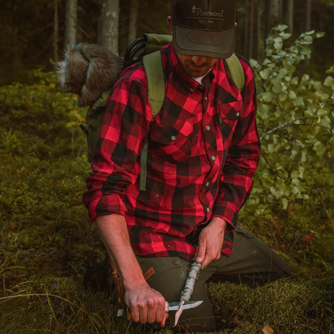 Person in Pinewood Lumbo Shirt, red and black plaid, holding an axe with a brown hat