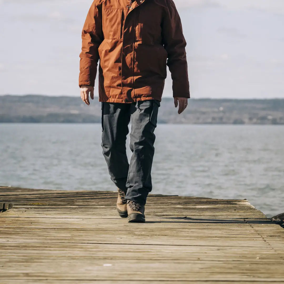 Person in a brown jacket and jeans on a dock, showcasing Pinewood Serengeti menswear for outdoors