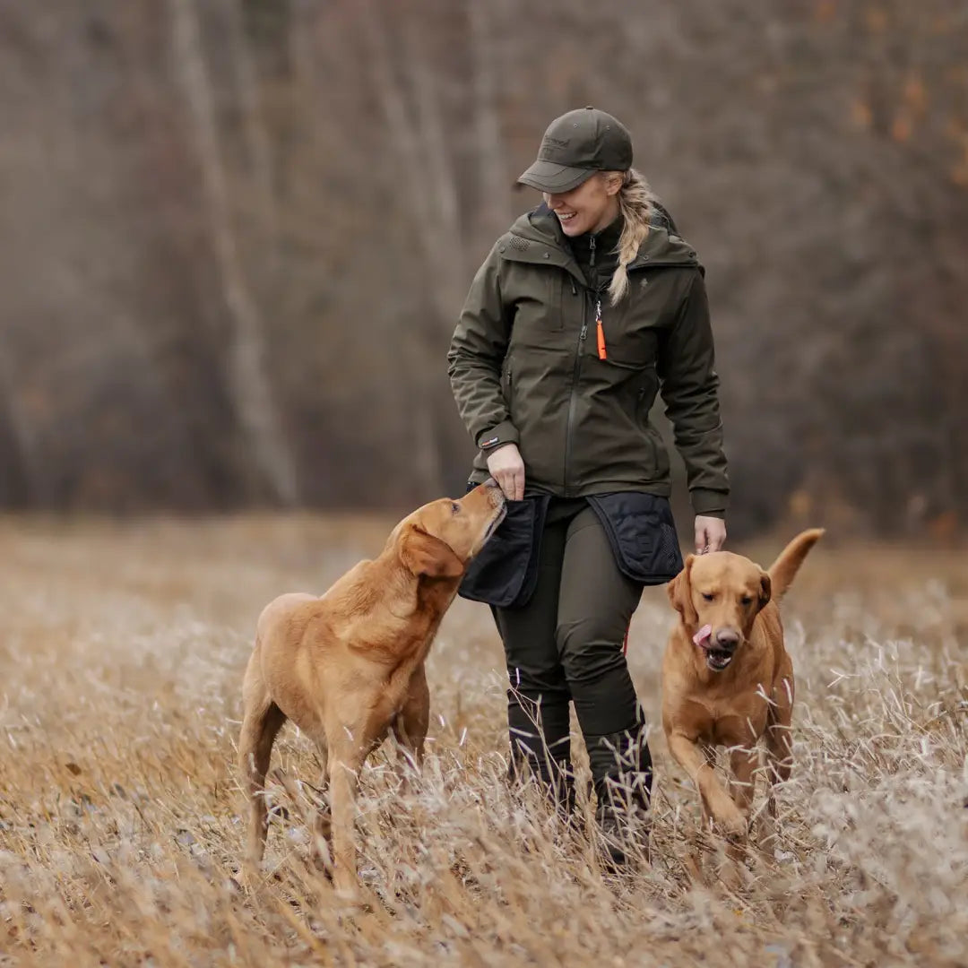 Person in Pinewood 3-layer jacket walks with two Golden Retrievers in a field