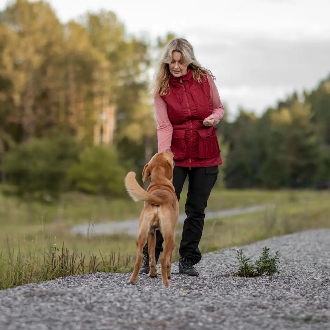 Woman in Pinewood Training Vest walks a golden dog on a cozy gravel path