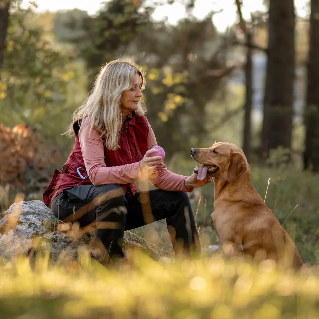 Woman in a Pinewood training vest relaxing outdoors with a golden retriever