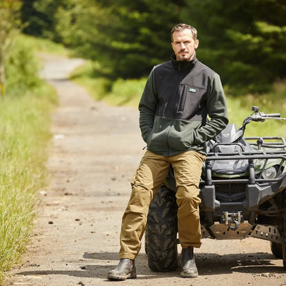 Man in Ridgeline Hybrid Men’s Fleece Jacket by an ATV on a dirt path, combines soft-shell