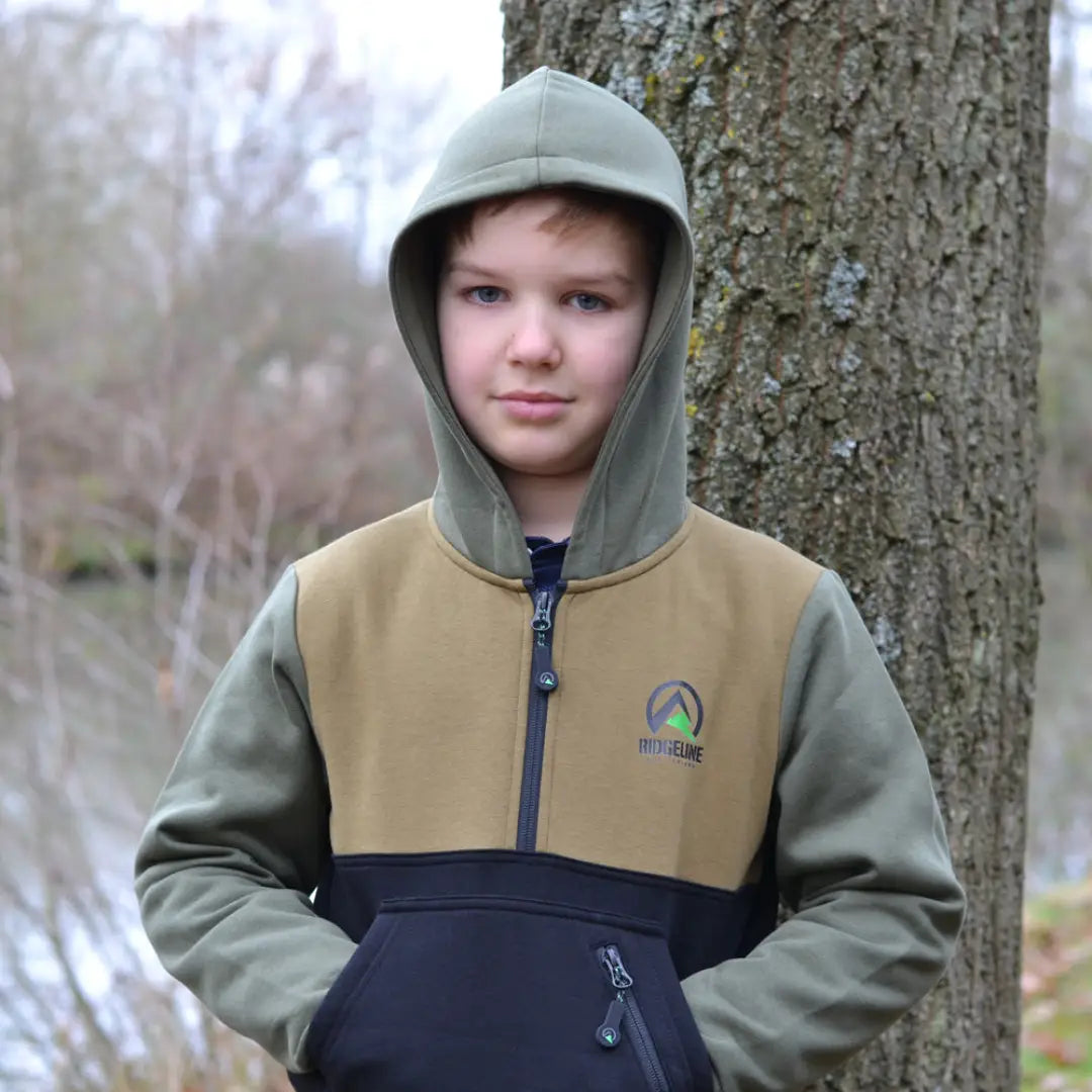 Child in a Ridgeline Kids Tribe Hoodie next to a tree trunk enjoying outdoor fun