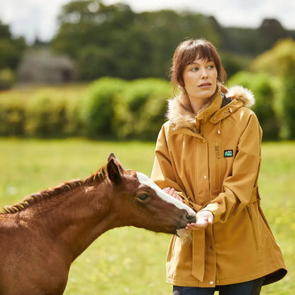 Woman in yellow jacket petting a brown foal, wearing a stylish Monsoon Nordic Jacket