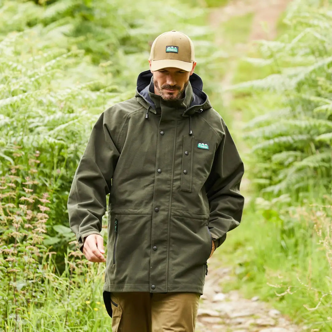 Man in a dark green Ridgeline Monsoon Classic jacket hiking on a fern-lined path