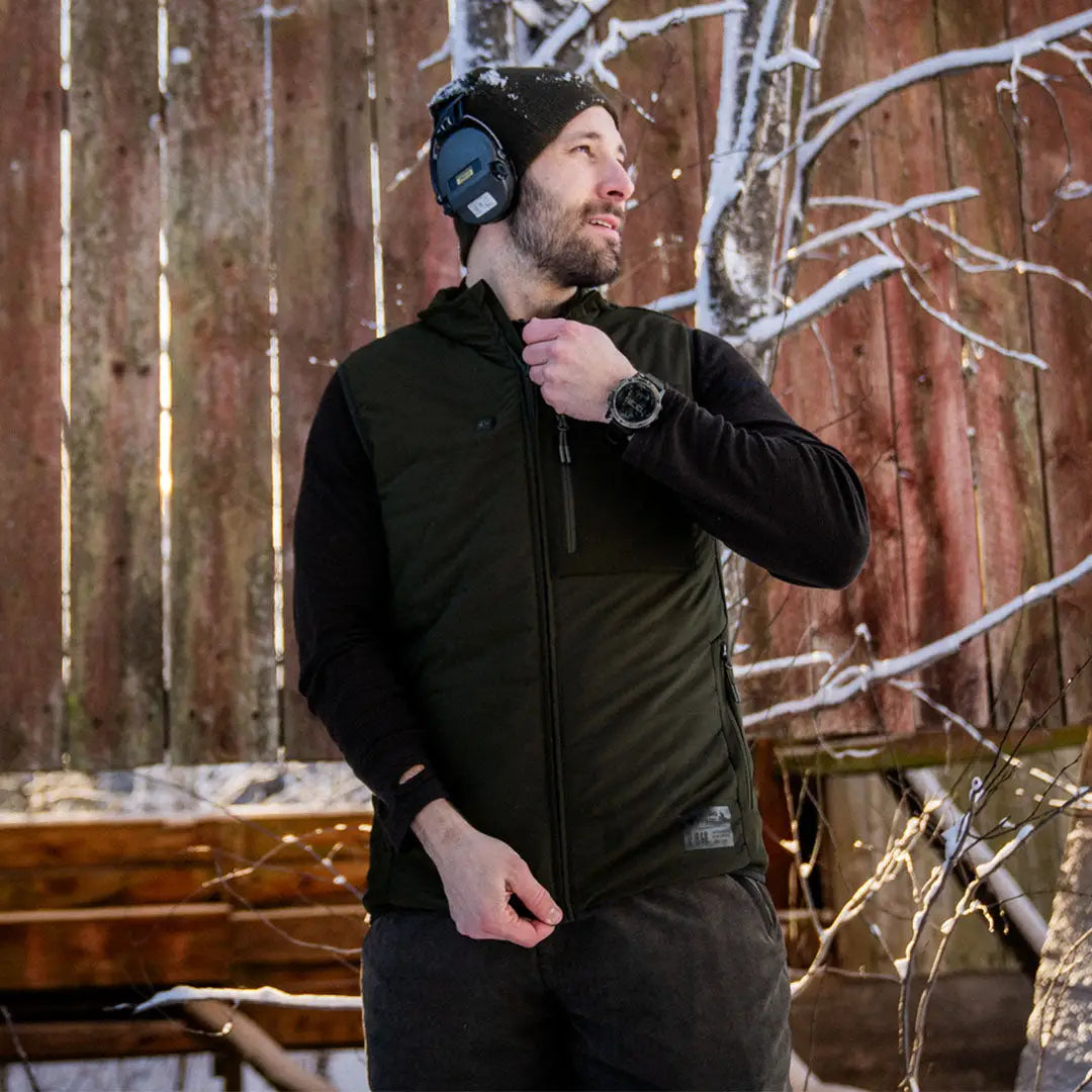 Bearded man in dark jacket and blue earmuffs wearing Celsius Heat Waistcoat in snow