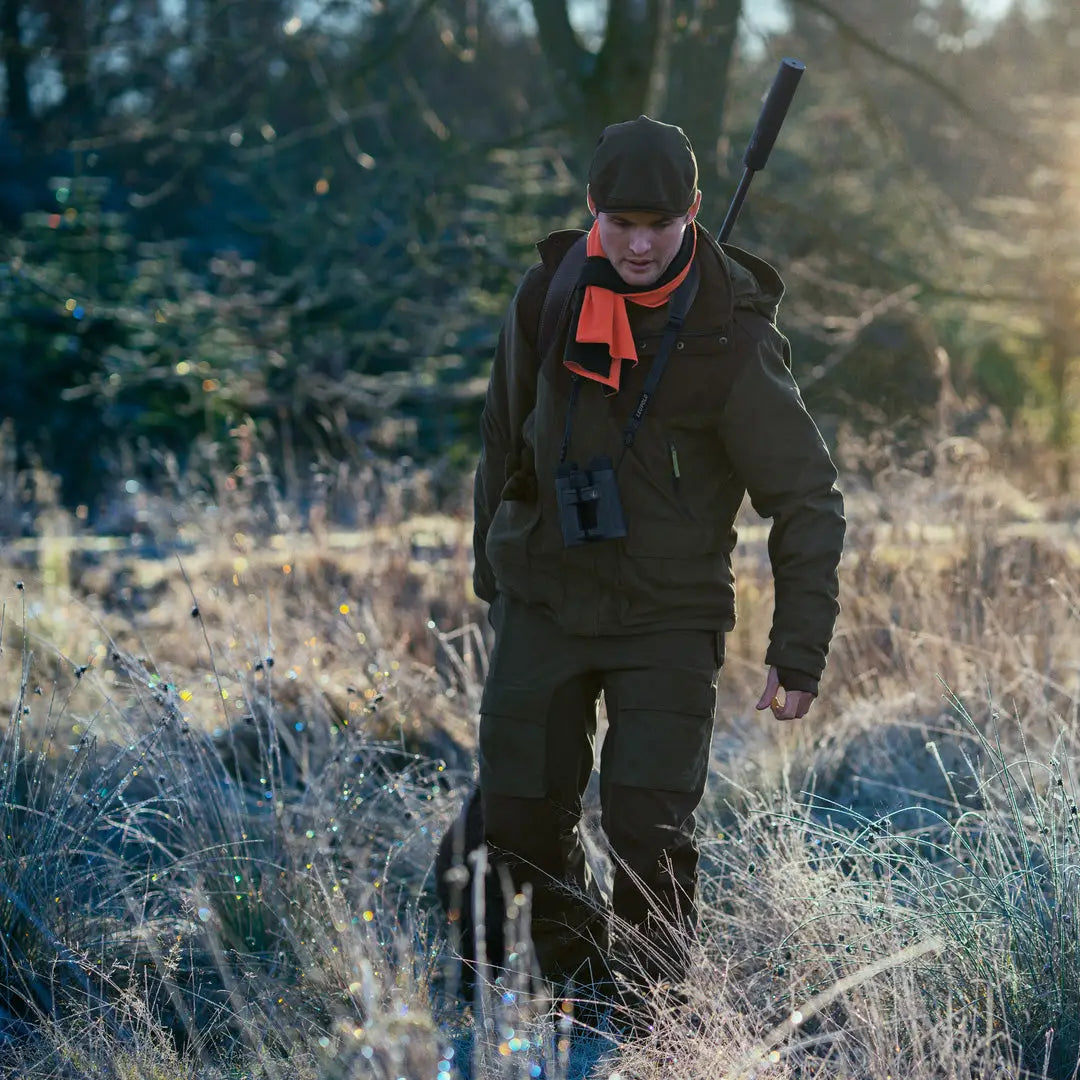 Hunter in Seeland Helt II Jacket walking through frosty grass with rifle and binoculars