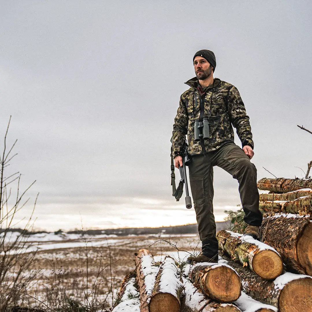 Man in camouflage wearing Seeland Rogue Reversible Fleece stands on logs