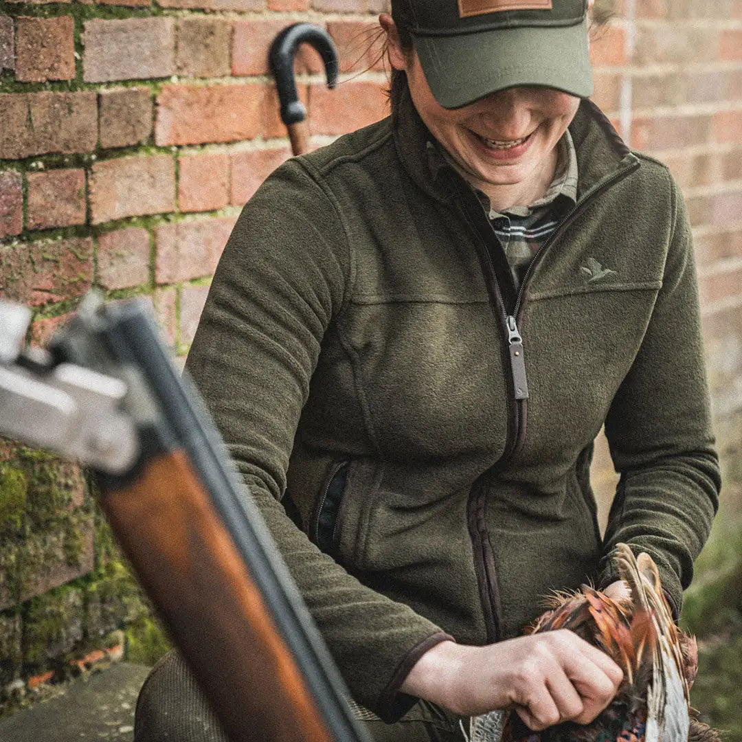 Person in a green Ivy Fleece Jacket and cap holding a shotgun outdoors