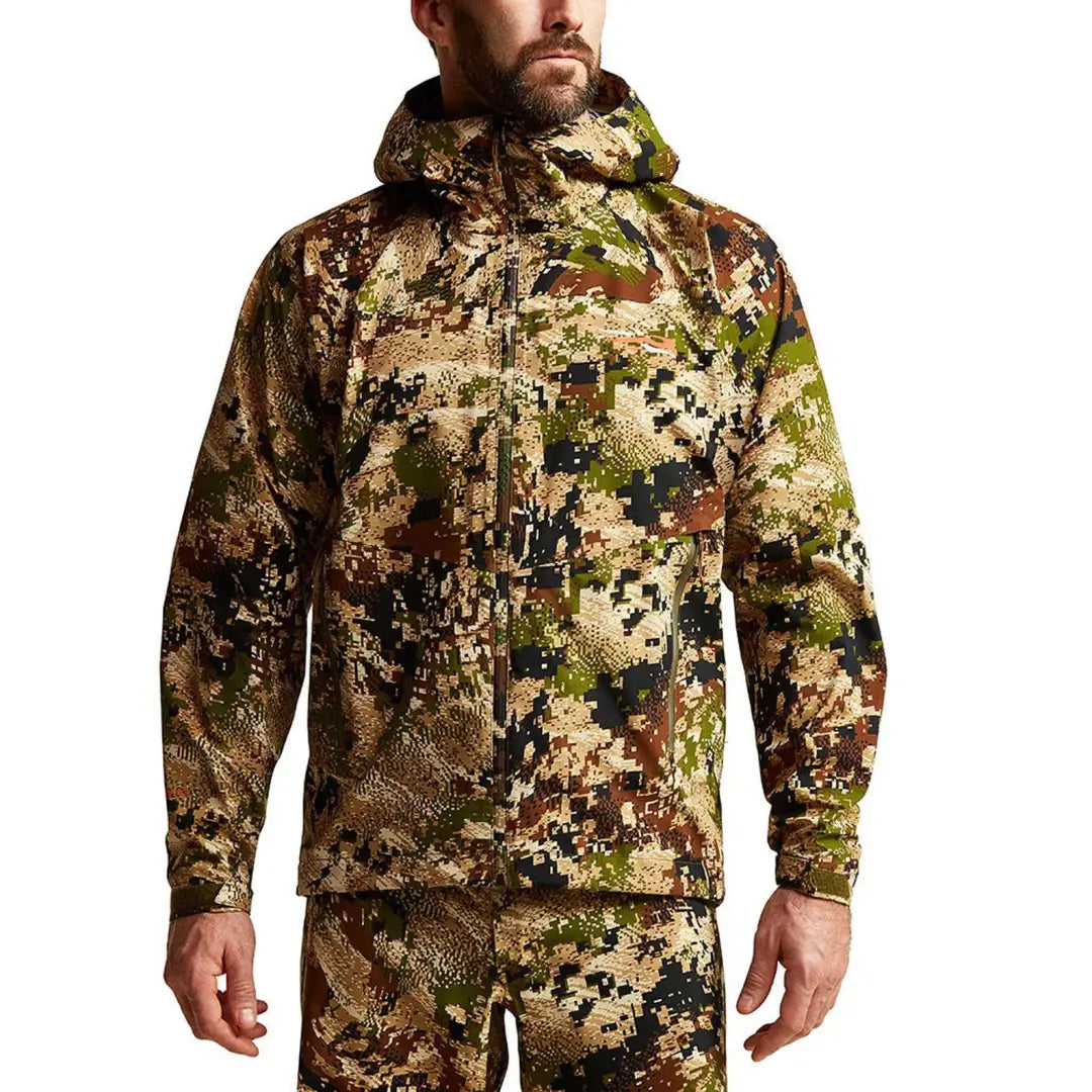 Person wearing a Sitka Dew Point Jacket in camouflage with a hood for hunting