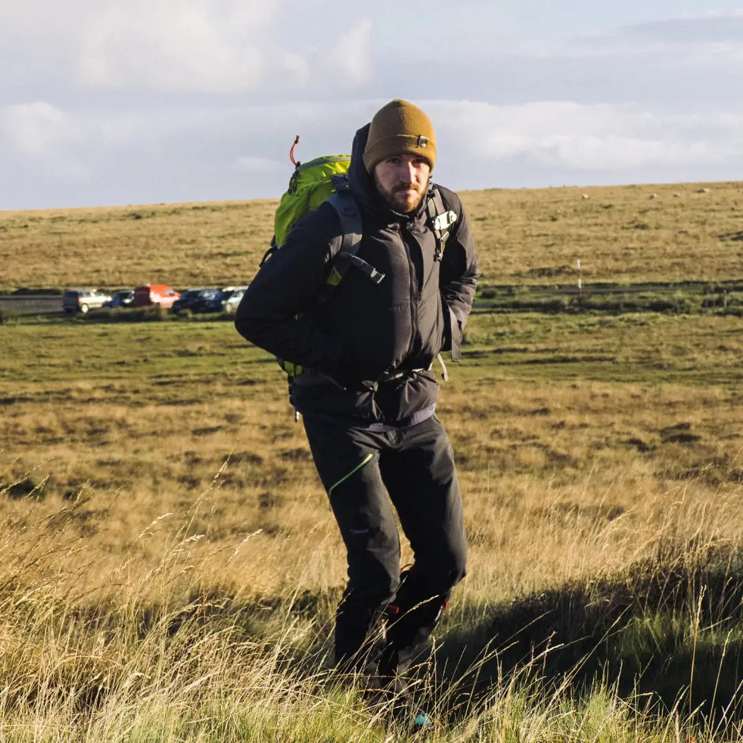 Hiker with a Snugpak Arrowhead Technical Insulated Jacket and green backpack in a field