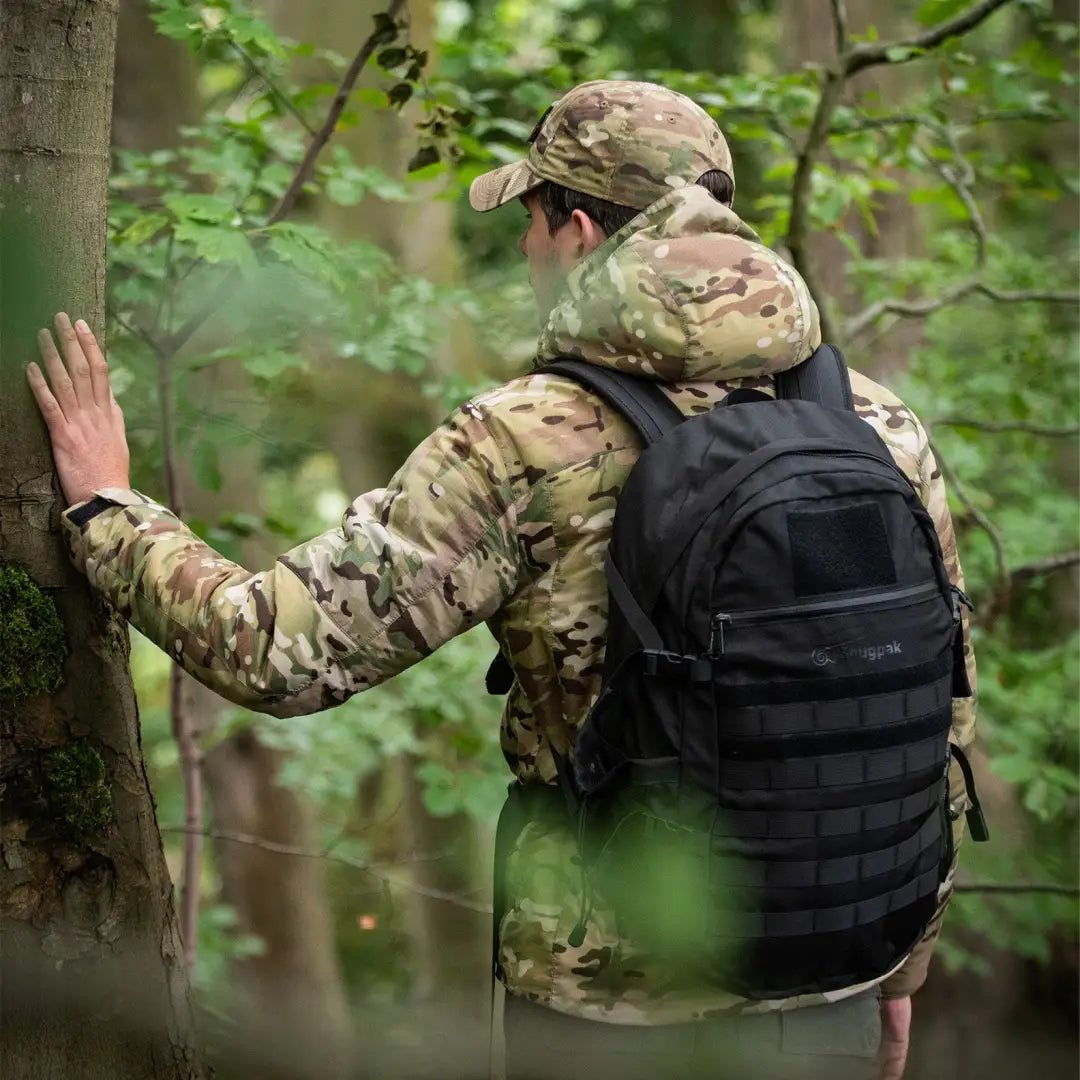 Soldier in camouflage wearing Arrowhead Technical Insulated Jacket touching tree trunk