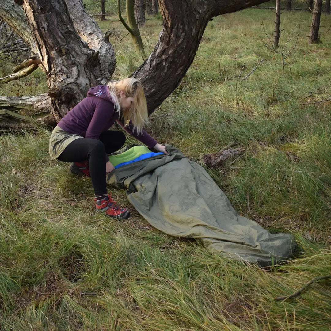 Person setting up a Snugpak Bivvi Bag near a gnarled tree for outdoor adventures